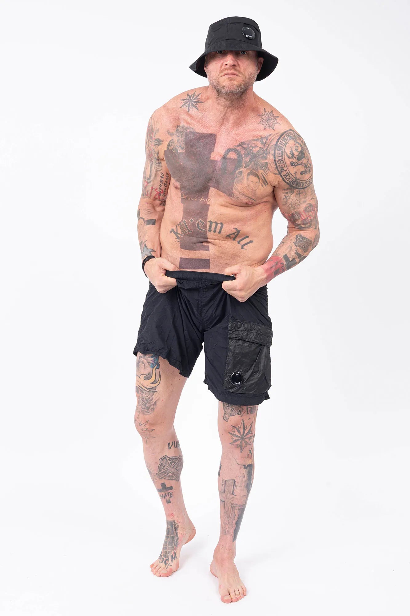 C.P. Company, Mens Swim Shorts, Black 999, Swimwear, Cargo Pockets, Elasticated Waistband, Quick-Dry Fabric, Polyamide, CP Company Signature Lens, Drawstring, Flatt Nylon, Wide Fit, Breathable, Full Body Front View with C.P. Company Bucket Hat. 