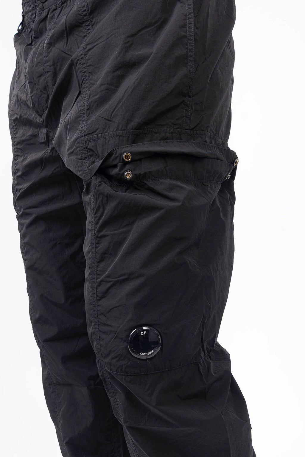 C.P. Company, Mens Pants, Black 999, Chrome-R Polyamide Nylon Trousers, Cargo Pockets, Side Pockets, Signature Lens, Lens Detail, Loose Fit, Straight Leg, Belt Loops, Zip-Fly, Button Closure, Back Pockets, British Saylor, Chester Perry, Massimo Osti, Front 3/4 Close-up View. 