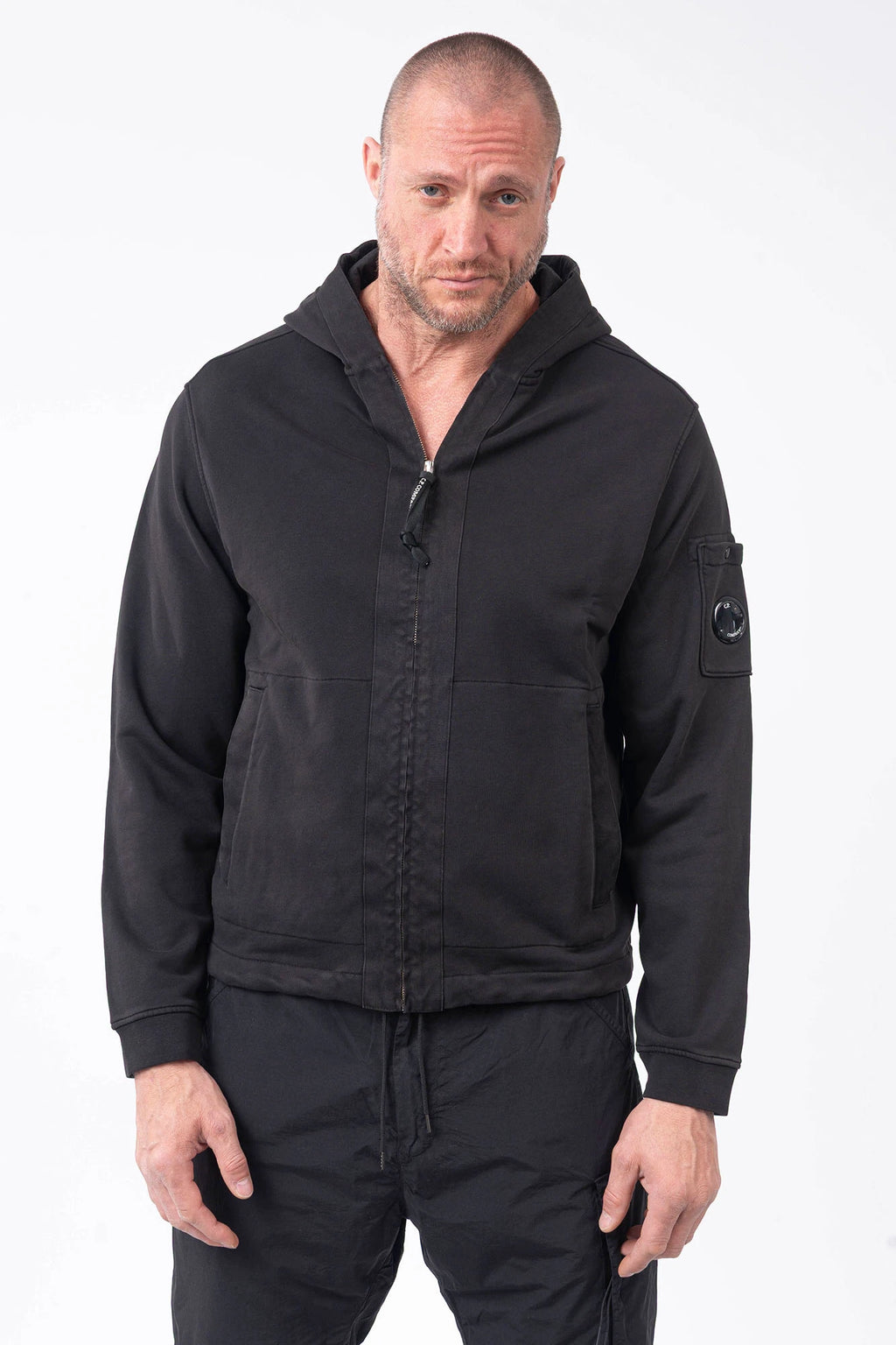C.P. Company, Mens Sweatshirt, Black 999, Full-Zip, Lens Sleeve Pocket, Hooded, Side Pockets, Ribbed and Cuffs, Cord Adjustable Hem, Snap Closure Sleeve Pocket, Signature C.P. Company Lens Detail, Chester Perry, British Saylor, Massimo Osti, Garment Dyeing Techniques, Front Portrait. 