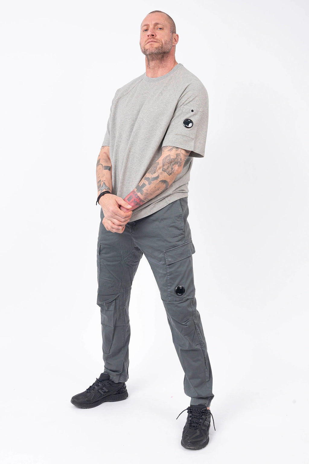 C.P. Company, Mens T-Shirt, Greystone Melange M94, Grey, Gray, Raglan Sleeves, Lens Sleeve Pocket, C.P. Company Signature Lens Detail, Cotton Fleece, Ribbed Hems and Neck, Tattoos, Massimo Osti, Chester Perry, C.P. Company Grey Cotton Cargo Pants, Full Body Front 3/4 View. 