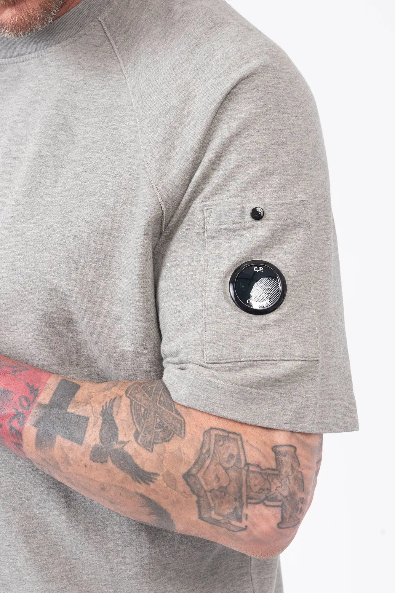 C.P. Company, Mens T-Shirt, Greystone Melange M94, Grey, Gray, Raglan Sleeves, Lens Sleeve Pocket, C.P. Company Signature Lens Detail, Cotton Fleece, Ribbed Hems and Neck, Tattoos, Massimo Osti, Chester Perry, C.P. Company Grey Cotton Cargo Pants, Sleeve Pocket Close-up. 