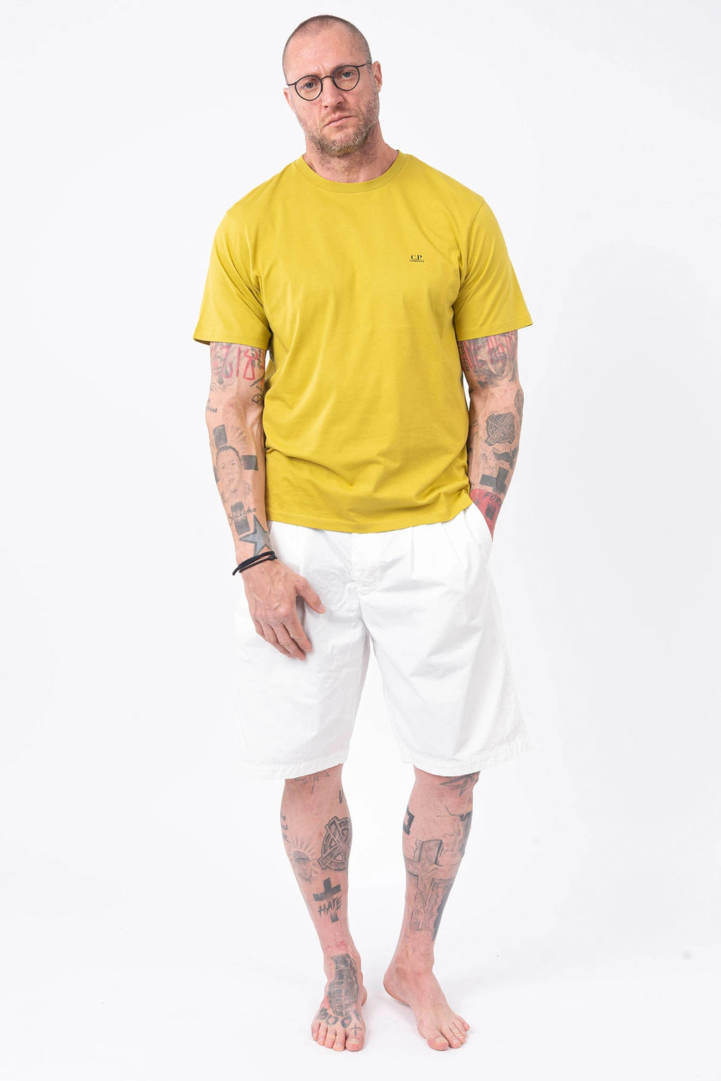 CP Company, Mens T-Shirt, Antique Moss, Yellow, Garment Dyed, Chest Logo Print, Back 'Goggles' Print, Short Sleeves, 100% Cotton, Ribbed Hems and Neck, Tattoos, Rigards Sunglasses, White CP Company Cotton Shorts, Full Body Front View. 