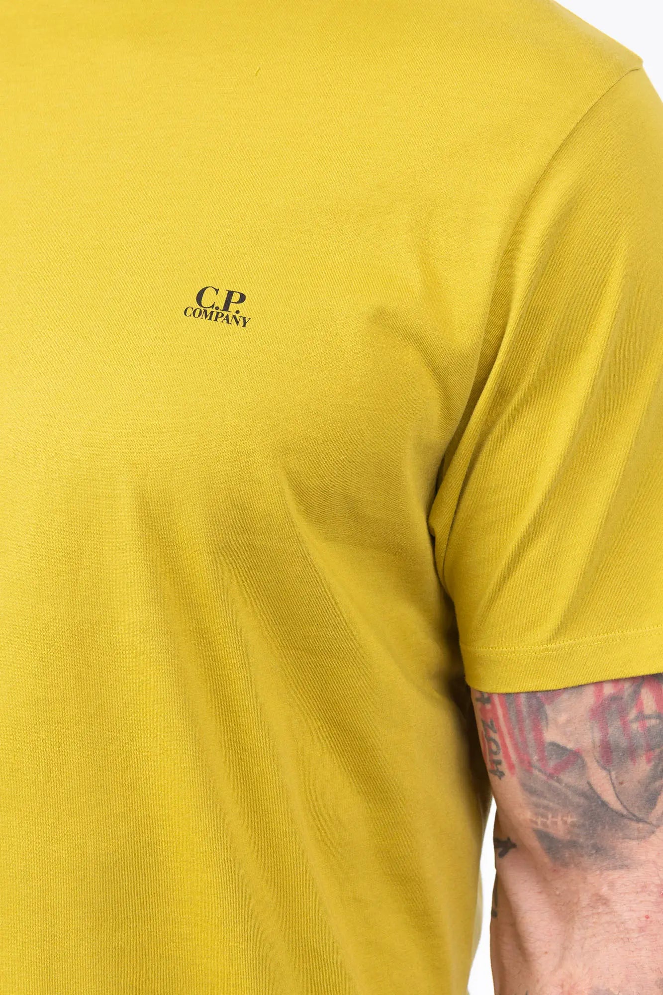 CP Company, Mens T-Shirt, Antique Moss, Yellow, Garment Dyed, Chest Logo Print, Back 'Goggles' Print, Short Sleeves, 100% Cotton, Ribbed Hems and Neck, Tattoos, Rigards Sunglasses, White CP Company Cotton Shorts, Chest Logo Close-up View. 