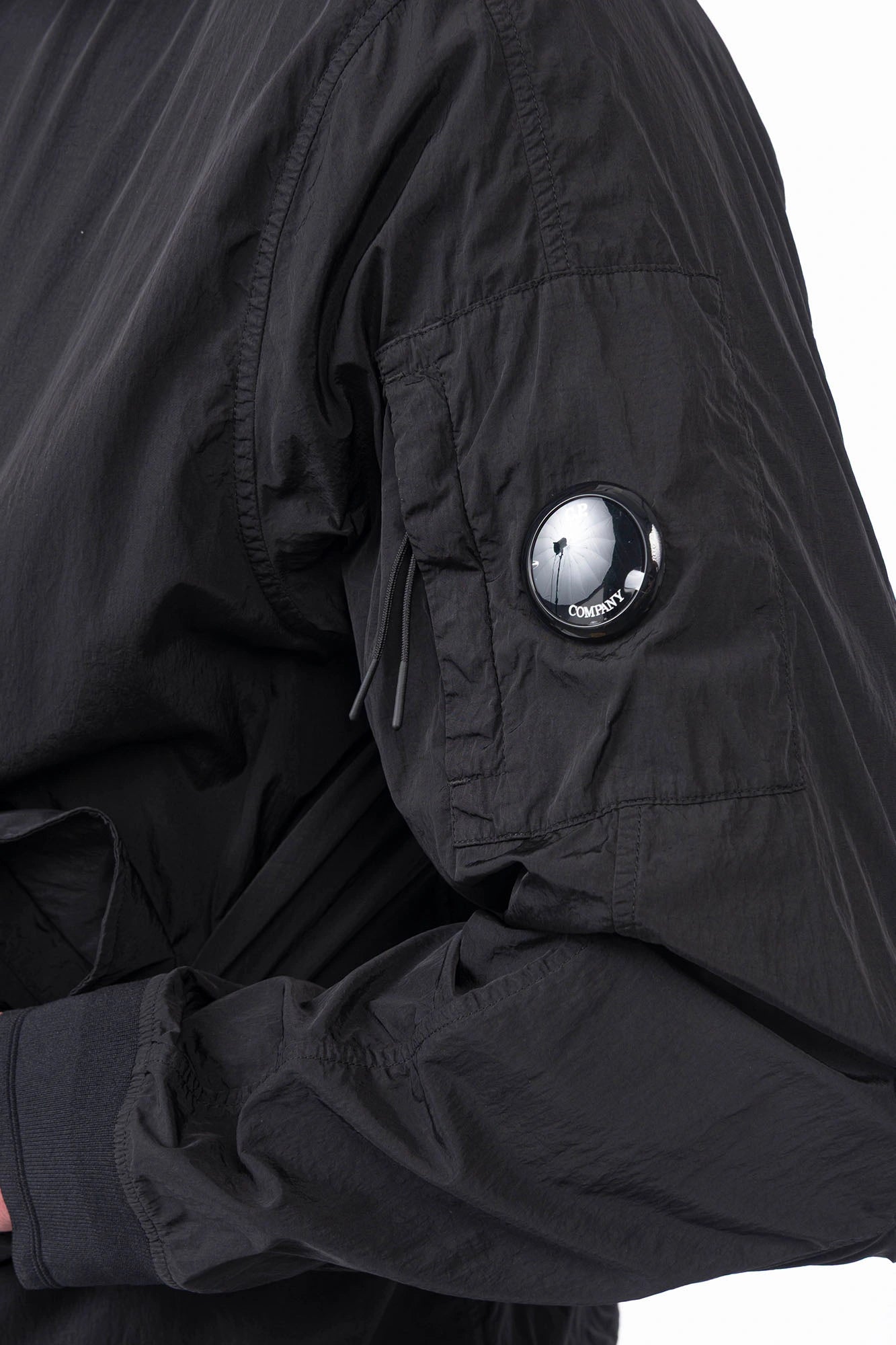 C.P. Company, Mens Jacket, Black 999, Concealed Hood, Chrome-R, Polyamide, Full-Zip, Side Flap Pockets, Sleeve Lens Pocket, Centre Zip Closure, Long Sleeves, Ribbed Elastic Cuffs, Branded Zip Puller, YKK Zippers, Two-Way Zipper, Sleeve Lens Detail Close-up. 