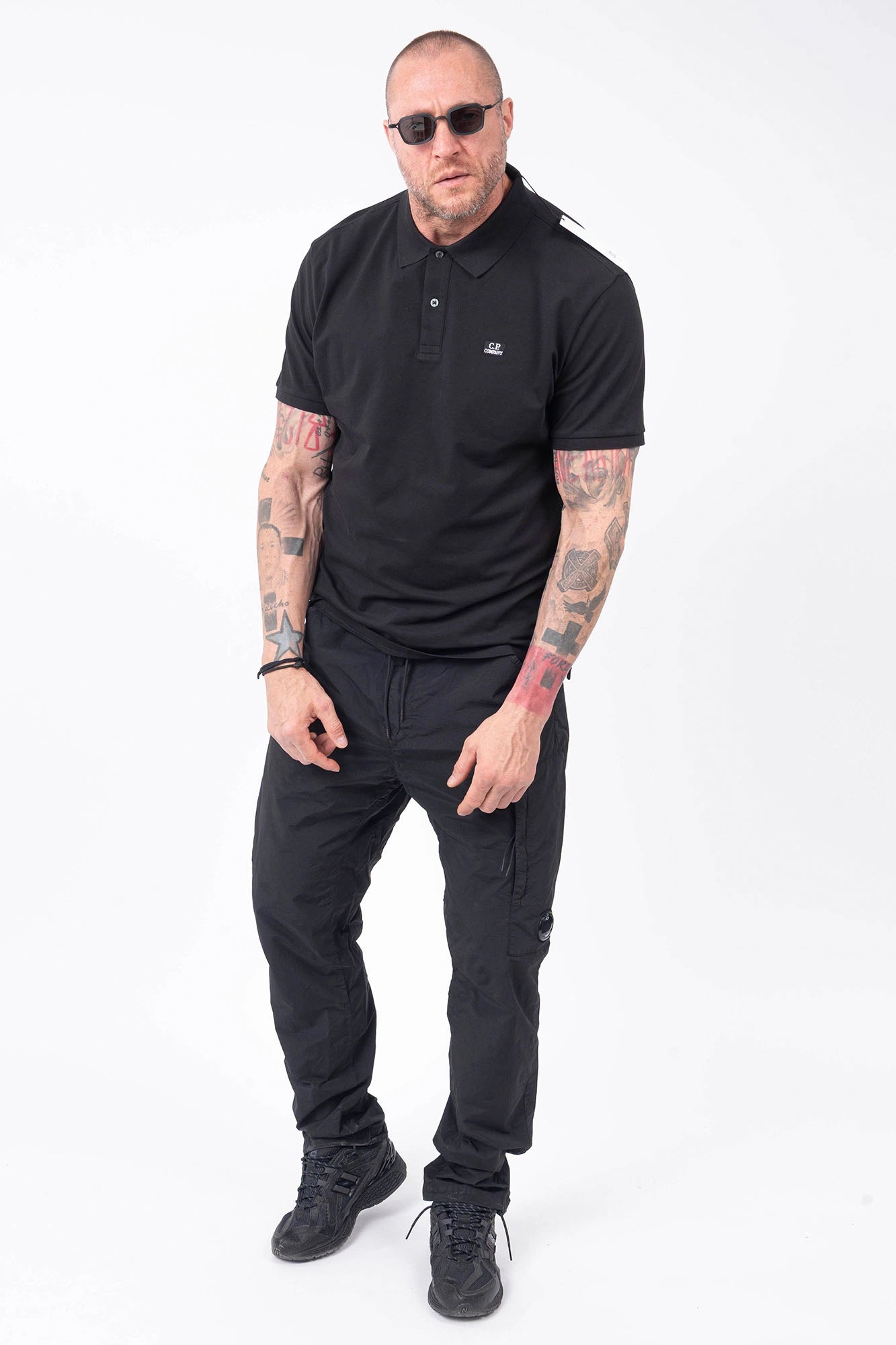 C.P. Company, Mens Polo Shirt, Black 999, Collar, Button Closure, Short Sleeves, Ribbed Hems, Stretch Cotton Pique, Chest Embroidery, Chester Perry, Massimo Osti, British Saylor, Rigards Sunglasses, Full Body Front View. 