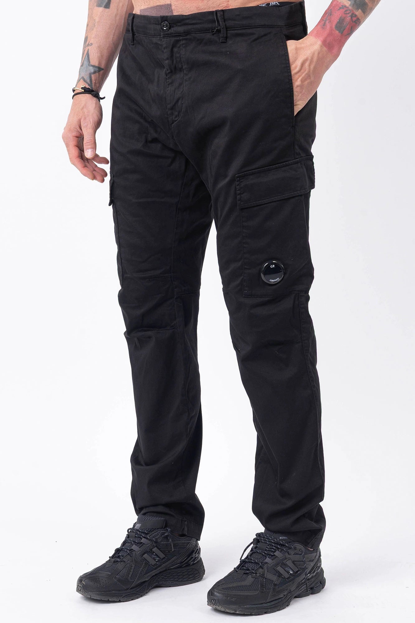 C.P. Company, Mens Pants, Black 999, Side Pockets, Cargo Flap Pockets, Lens Pocket Detail, Belt Loops, Button Closure, Zip-fly, Back Pockets, Stretch Cotton Sateen, Massimo Osti, Chester Perry, British Saylor, Front 3/4 View Hand in Pocket. 