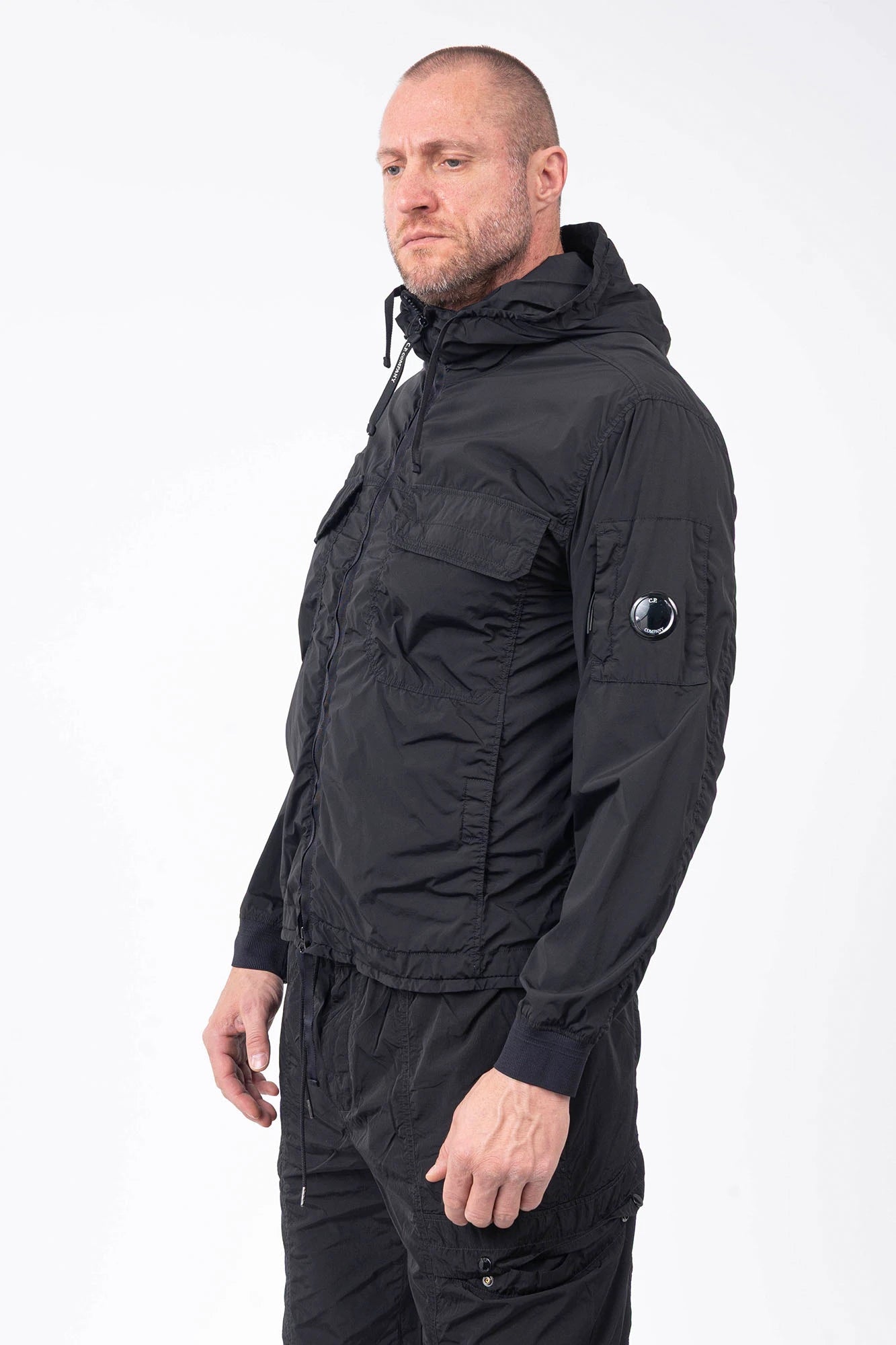 C.P. Company, Mens Jacket, Black 999, Stretch Nylon, Shell-R, Nycra-R, Hooded, Water-Resistant, Wind-Resistant, Windproof, Waterproof, Full-Zip, Centre Zip Closure, Bellow Pockets, Side Pockets, Sleeve Pocket, Massimo Osti, Chester Perry, Front Portrait 3/4 View. 
