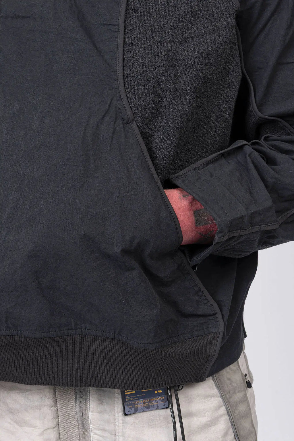 Hamcus, Mens Pullover, Matte Black, Dark Grey, Dark Gray, Half-Zip, Quarter-Zip, Long Sleeves, Mock Neck, Symmetric Panel Design, Ribbed Hem and Sleeve Cuffs, Side Pockets, Elastic Drawcord Adjustable Cuffs with Cordstoppers, Ribbed Neck, Back LP World Print, Left Hand in Pocket Close-up View. 