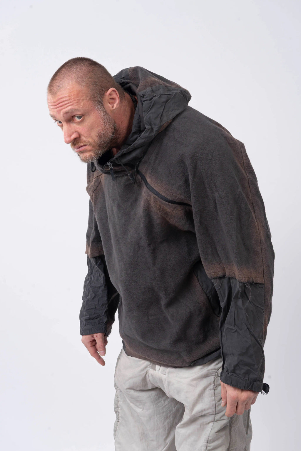 Hamcus, Mens Hoodie, Star-Scorched Black, Brown Details, Sun-Faded, Multiple Ventilation Zipper Openings, Hooded, Adjustable Drawcord Hood, Multi-Fabric Blend, LP World, Lower Planetary Universe, Tattoos, Raw-Cut Details, Elasticated Cuffs, Front 3/4 View Leaning Over Looking Directly at the Camera. 