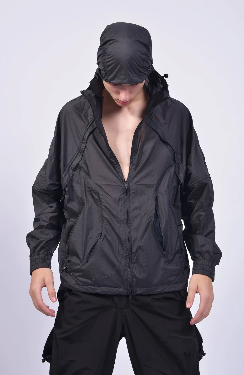 Nilmance, Mens Jacket, Transparent, Light Grey, Gray, Full Zip, Zip Ventilation Openings, Elasticated Cuffs, Cinch Hood, Drawcord Hood, Side Zip Pockets, Lightweight, Windproof, Front Portrait Hooded Looking Down. 
