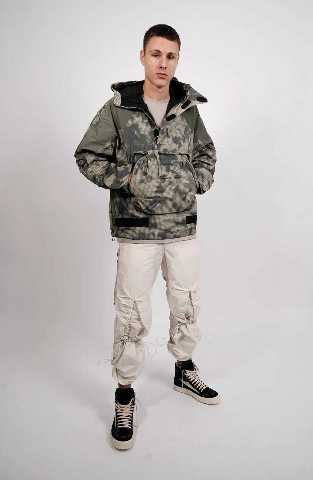 Nilmance, Mens Jacket, Green Camo, Elastic Concealed Drawcord Hood and Hem, Velcro Adjustable Cuffs and Hood, Large Front Zip Pocket, YKK Zippers, Ripstop Nylon, Water-repellent treated, Full Body Front 3/4 View Hands in Pockets. 