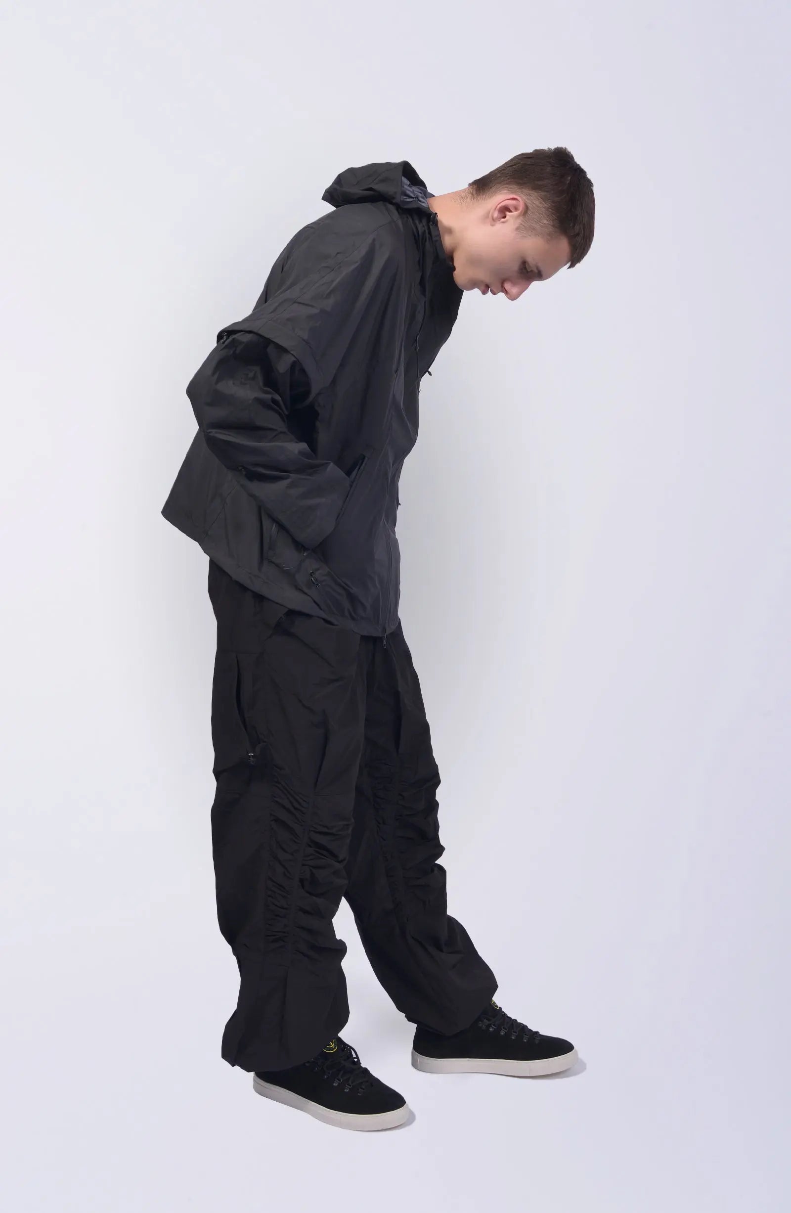 Nilmance, Mens Jacket, Black, Waterproof 10k, Windproof, Water-Repellent, Full-Zip, Zip Pockets, Side Pockets, Hidden Pockets, Detachable Sleeves, Velcro Adjustable Cuffs, Drawcord Hood, Cinch Hood, Zip Ventilation Openings, Side View Bent Forward Looking Down. 
