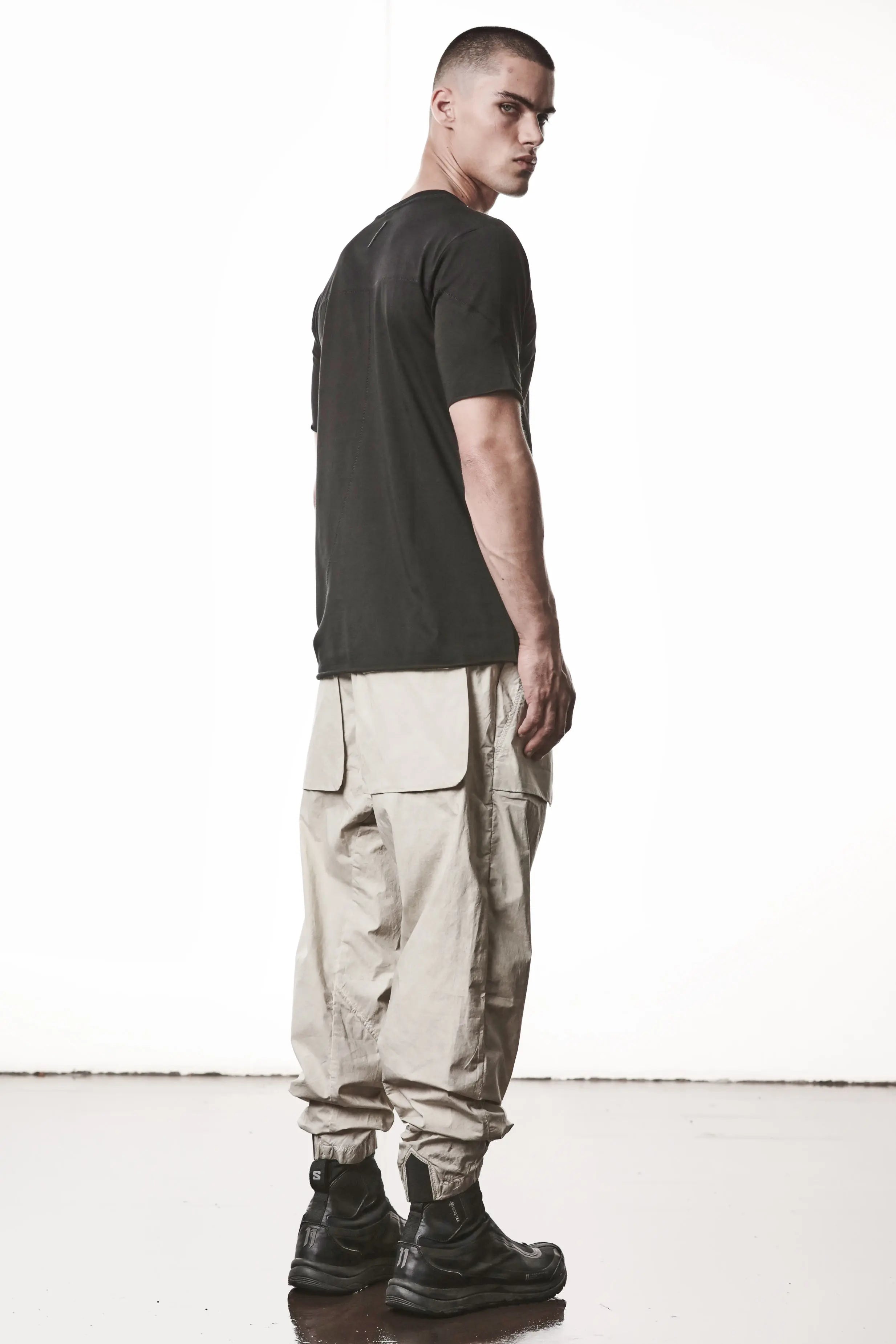 Thom Krom, Mens T-Shirt, Black, Raw-Cut Hem, Elastic Neck, 100% Cotton, Short Sleeves, Crewneck, Round Neck, White Cross Seams, Back Seams, Embroidered Logo, Full Body Back 3/4 View. 