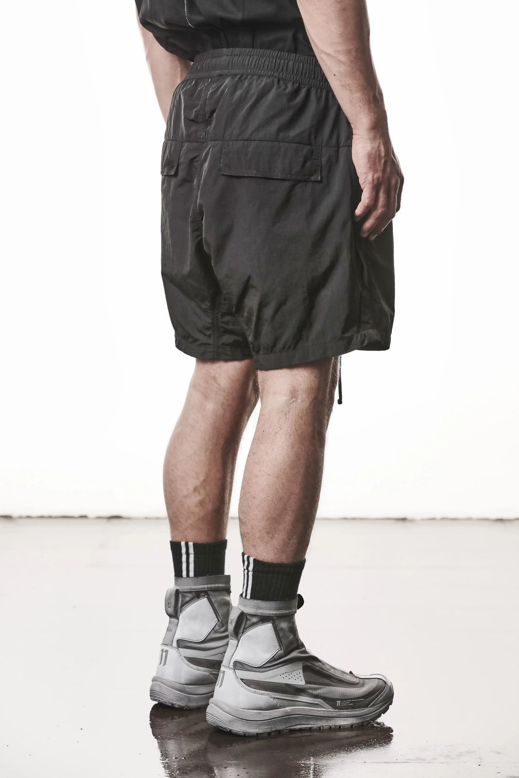 Thom Krom, Mens Shorts, Black, Polyamide, Side Pockets, Elasticated Waistband, Drawsting, Cross Seams, Wide Fit, Over the Knee Legs, Drop-Crotch, Hidden Zip Pockets, Back 3/4 View. 