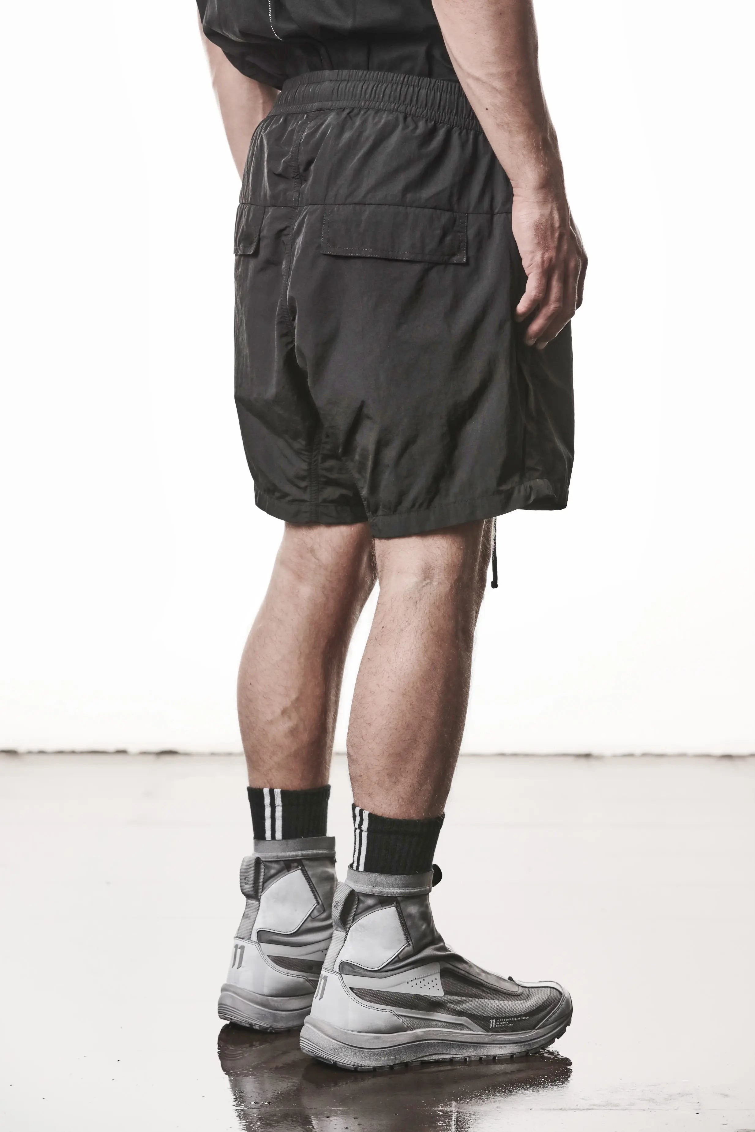 Thom Krom, Mens Shorts, Black, Polyamide, Side Pockets, Elasticated Waistband, Drawsting, Cross Seams, Wide Fit, Over the Knee Legs, Drop-Crotch, Hidden Zip Pockets, Back 3/4 View. 