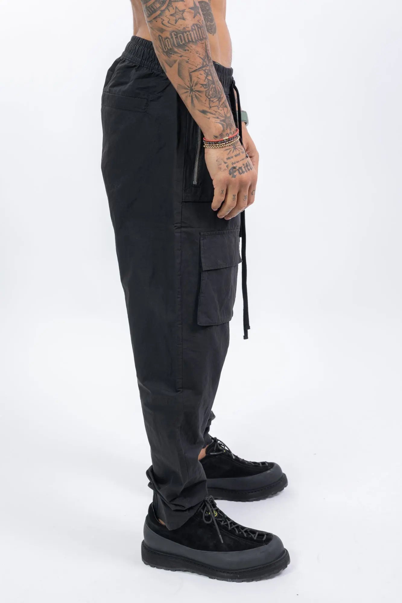 Thom Krom,Mens Trousers,Relaxed Fit,Mid-Rise Waist,Drop Crotch,Tapered Leg,Elastic Waistband With Adjustable Drawstring,Concealed Button Placket With Logo Buttons At The Front,Two Patch Bellows Pockets With Zipper On The Front,Two Patch Bellow pockets With Flaps On The Front,Welt Pocket 
And Patch Bellows Pocket With Flap On The Back,Security Pocket With Zipper On The Inside,Leg Hem With Elastic Insert On The Back, Profile View.