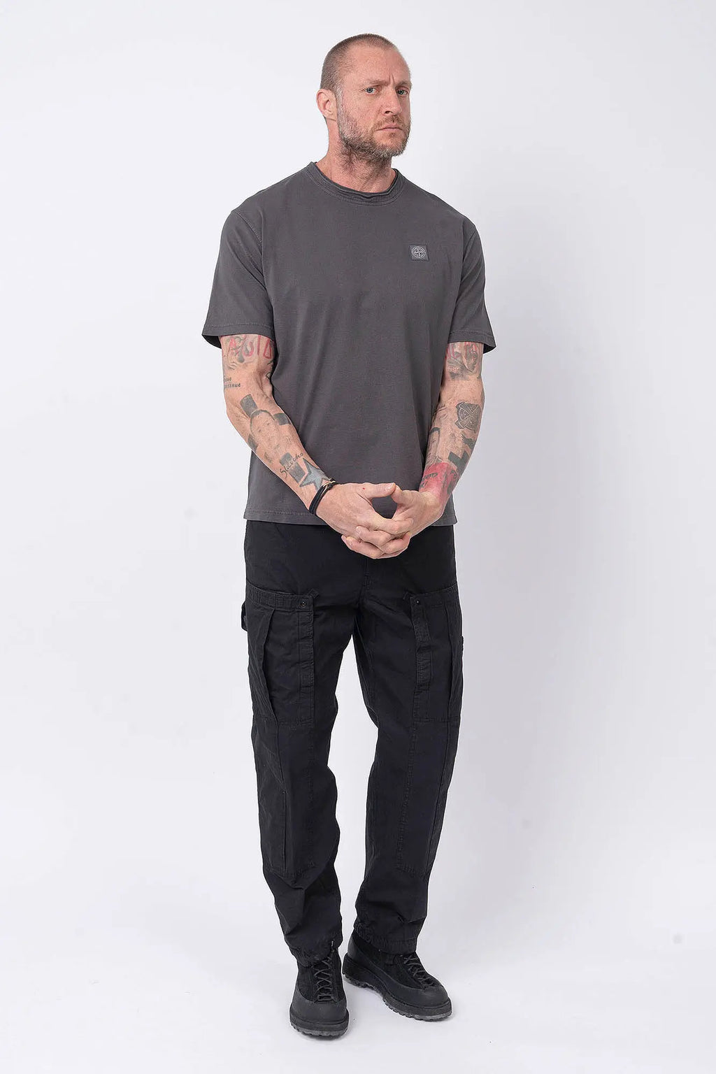 Stone Island, Mens T-Shirt, Charcoal V0165, Grey, Gray, Garment Dyed, Short Sleeves, Elastic Ribbing, Organic Cotton, Wide Fit, Raw-cut Neck, Crewneck, Round Neck, Compass Badge, Logo-patch, Chest Compass Patch, Full Body Hands Clasped Front View. 