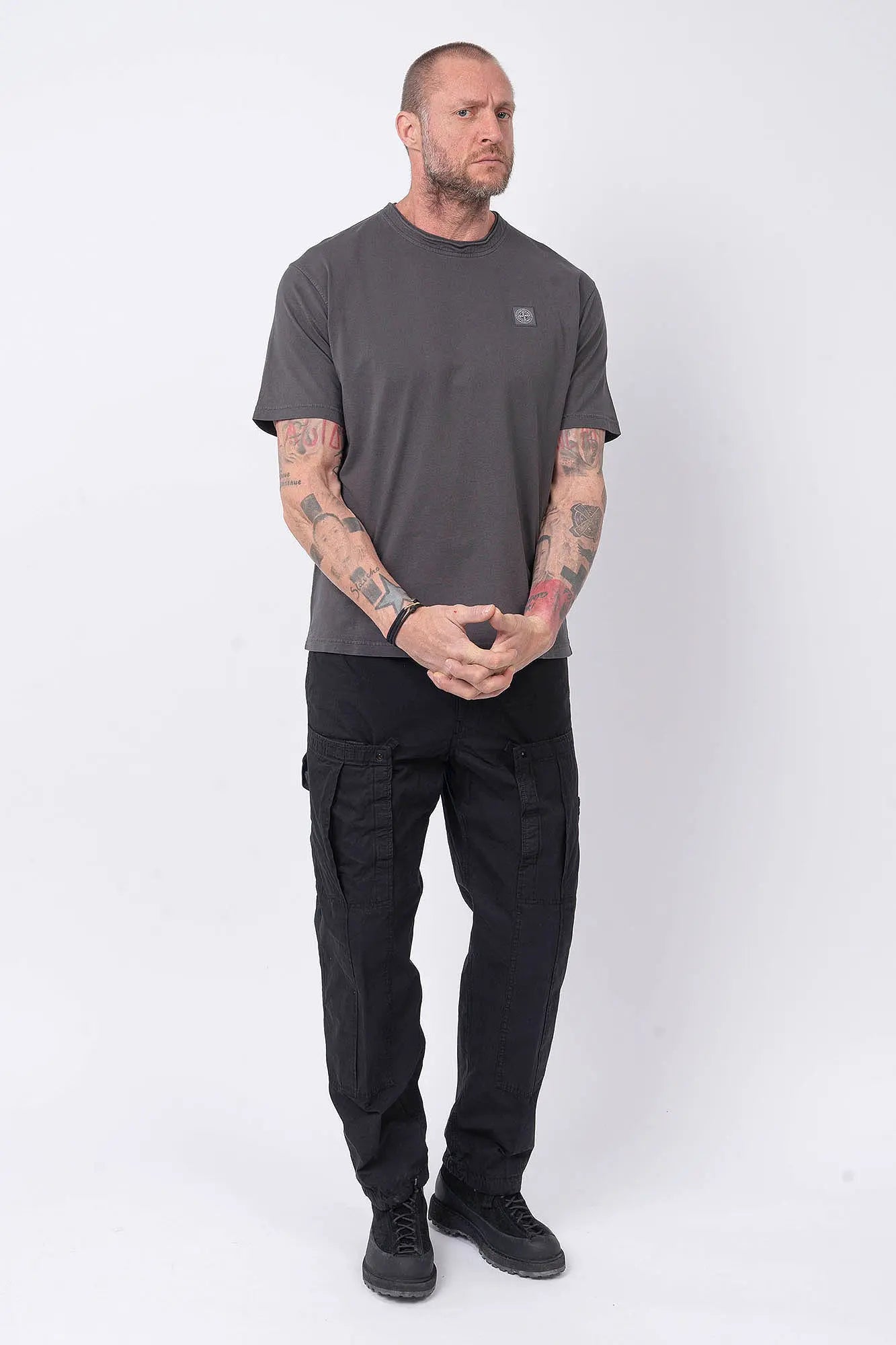 Stone Island, Mens T-Shirt, Charcoal V0165, Grey, Gray, Garment Dyed, Short Sleeves, Elastic Ribbing, Organic Cotton, Wide Fit, Raw-cut Neck, Crewneck, Round Neck, Compass Badge, Logo-patch, Chest Compass Patch, Full Body Hands Clasped Front View. 